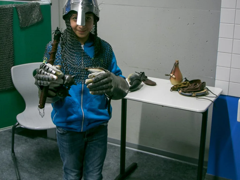 Kind in Kettenhemd und Helm hält eine Waffe.